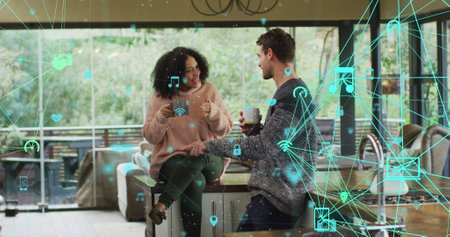Image of network of media icons over happy biracial couple having coffee talking at home. global communication and digital interface technology lifestyle concept digitally generated image.の写真素材