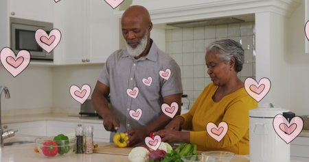 Image of pink hearts over happy african american senior couple preparing food in kitchen. senior life, retirement and golden years concept digitally generated image.の写真素材