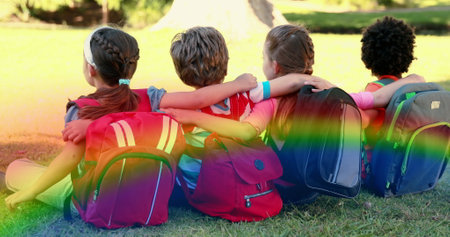 Image of rainbow fog over diverse children sitting on grass. find a rainbow day digitally generated...