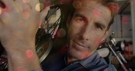 Image of flickering lights over caucasian male mechanic holding motorcycle wheel. motorcycle safety...