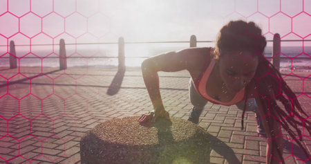 Pink hexagonal shapes against t african american fit woman performing push ups on the promenade....