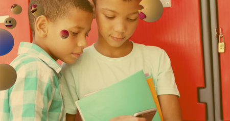 Image of emojis icons over diverse schoolboys using smartphone. national telephone day, technology and communication concept digitally generated image.の写真素材