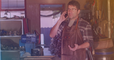 Image of caucasian male worker talking on smartphone in workshop. work and business concept digitally generated image.の写真素材