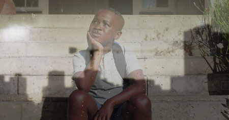 Image of cityscape over sad african american boy sitting on stairs. childhood, loneliness, emotions...