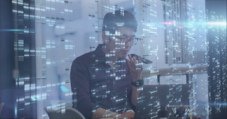 Blue spot of light and mosaic squares against asian man using laptop at office.