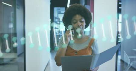Dna structure spinning against african american woman talking on smartphone and walking at office. business and medical research technology conceptの写真素材