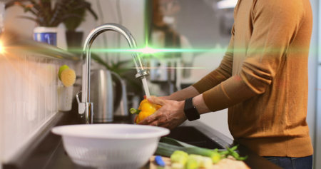 Image of light moving over midsection of man washing vegetables in kitchen. everyday life, spending...