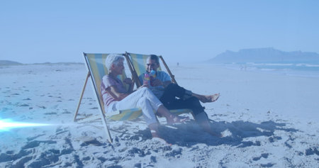 Image of light spots over senior biracial couple lying on sunbeds. national relaxation day and celebration concept digitally generated image.の写真素材