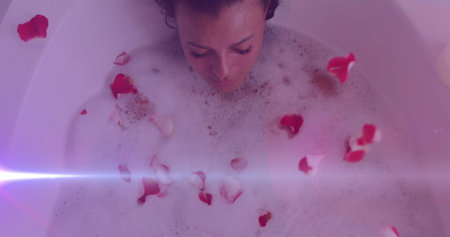 Image of light spots over caucasian woman taking bath with petals. national relaxation day and celebration concept digitally generated image.の写真素材