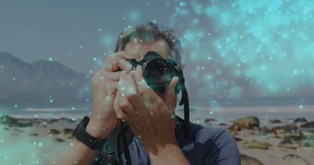 Blue glowing spots against caucasian senior male photographer clicking pictures with digital camera. world photo day awareness conceptの写真素材