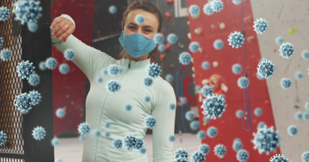 Raising arm woman in teal top mask at climbing gym, with red walls and virus graphics. Fitness, health, activewear, indoor recreation, motivation, wellness, sportの写真素材