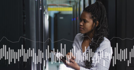 Image of graphs and data over african american woman in server room. network, programming, computers and technology concept digitally generated image.の写真素材