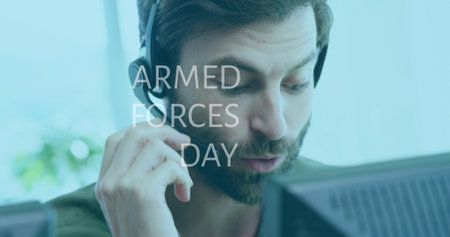Talking bearded man wearing headset using microphone at desk, with computer monitor and plant. Technology, communication, workspace, modern, professional, focused, digitalの写真素材