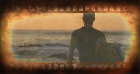Standing man in wetsuit holding surfboard, facing ocean on beach at dusk with filmstrip effect....