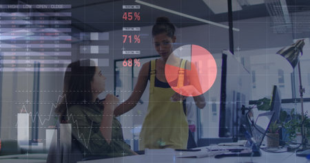 Statistical data processing against two diverse female office colleagues discussing at office....