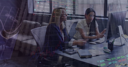 Statistical data processing against two diverse female office colleagues discussing at office. Business analytics and data technology conceptの写真素材