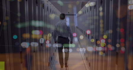Walking IT technician wearing shirt navigating data center aisle with LED lights on server racks....