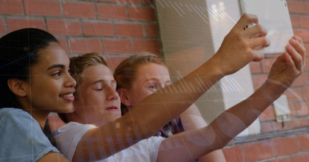 Image of financial graph over happy diverse pupils taking selfie at school. School, education, learning, finance and economy concept digitally generated image.の写真素材