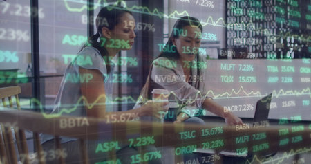 Image of financial data and graphs over diverse female coworkers in office. Business, finance, economy, cooperation and communication concept digitally generated image.の写真素材