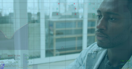 Image of financial graphs and data over african american man using laptop in office. Business, finance and economy concept digitally generated image.の写真素材