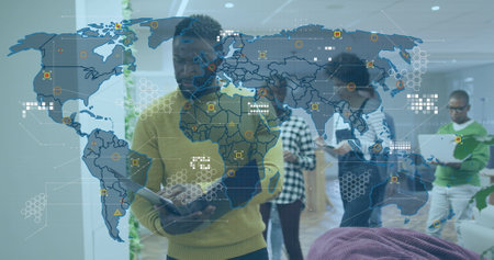 Image of world map and icons over african american man working in office. Business, finance, economy and technology concept digitally generated image.の写真素材
