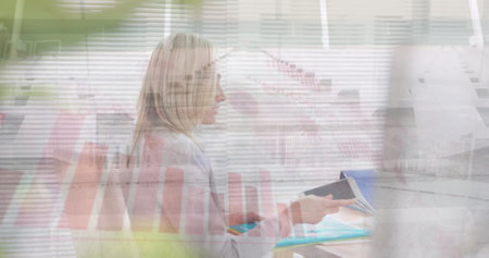 Image of caucasian businesswoman working at desk over graphs. digital composite, multiple exposure, entrepreneur, report, profession and technology concept.の写真素材