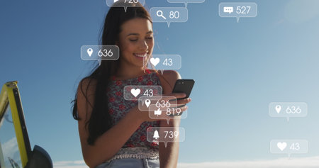 Image of social media reactions over happy caucasian woman with smartphone on beach. Network, connections, holidays and relax concept digitally generated image.の写真素材
