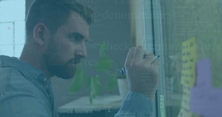 Image of data processing against caucasian man writing on memo notes at office. Computer interface...