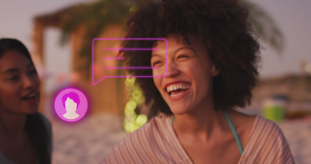 Image of profile icon with speech bubble over two diverse female friends smiling at the beach....