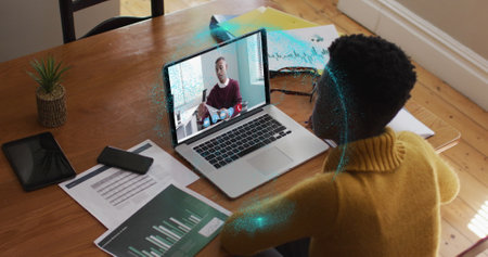 Image of spinning globe over african american woman having a image call on laptop at home. Global networking and business technology conceptの写真素材