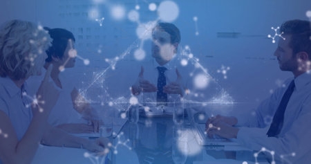 Talking male in white shirt and tie gesturing at conference table with laptops network-node overlay....