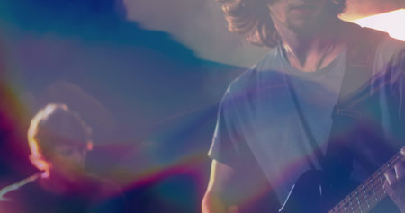 Playing guitarist strumming strapped electric guitar onstage with haze and stage lights, copy space. Musicians, performance, entertainment, stage, ambiance, lighting, creativityの写真素材