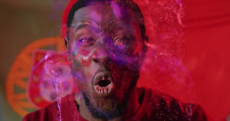 Shouting red shirt man showing flag face paint emitting magenta purple powder on set, sports crest. Dynamic, expressive, celebration, energy, motion, vibrant, athleticの写真素材