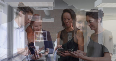Seven professionals standing near window in modern workspace, sharing smartphone and tablet screens. Collaboration, teamwork, technology, modernity, business, startup, communicationの写真素材
