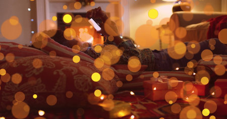 Lying girl using smartphone on patterned rug in festive room, with string lights and gift boxes....