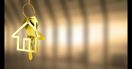 Hanging house-shaped golden key ring holding two metallic keys in softly lit corridor, copy space. Luxury, elegance, craftsmanship, jewelry, decorative, urban, sophisticatedの写真素材