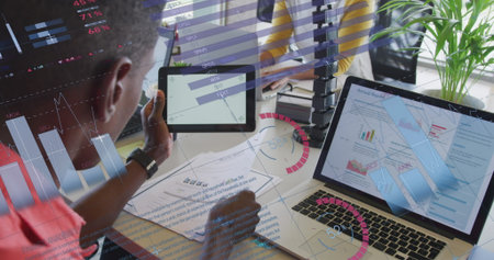 Reviewing coworker holding tablet and stylus pen at office desk with laptop and plant, copy space....