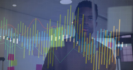Black man wearing brown sweater studying digital charts on glass wall in office, with sticky notes. Business intelligence, data analysis, analytics, innovation, modern workspace, technology, collaborationの写真素材