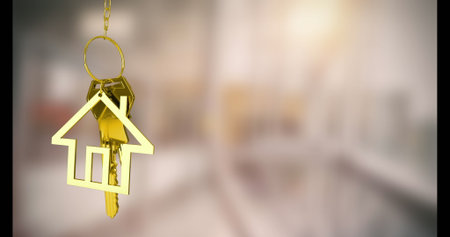 Hanging gold house-shaped keychain with metallic keys in hallway interior, with warm home concept. Accessories, luxury, minimalist, interior, decor, lifestyle, eleganceの写真素材