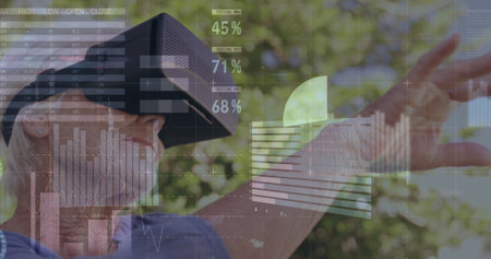 Senior woman wearing blue shirt and VR headset touching digital graphs in garden, copy space....