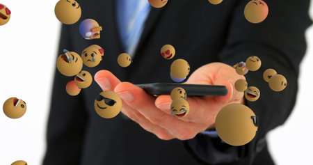 Extending hand of businessman in black suit holding smartphone in studio, with floating emoji icons. Professional, technology, communication, expression, innovation, digital, corporateの写真素材