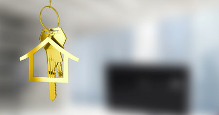 Hanging house-shaped keychain holding gold keys on gold keyring in home office, copy space. Luxury, elegance, minimalist, security, organization, decor, metallicの写真素材