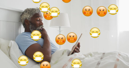Reading man wearing blue shirt holding tablet in bedroom, with lamp and emoji icons, copy space. Relaxation, technology, comfort, casual, sleep, interior, digitalの写真素材