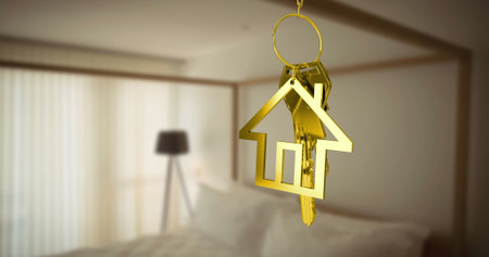 Dangling gold keyring showing house-shaped pendant and metal keys in bedroom, white linens and lamp. Jewelry, home, interior, decor, luxury, elegance, tranquilityの写真素材