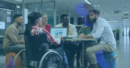 Six office professionals collaborating around meeting table in office, with laptop and wheelchair....