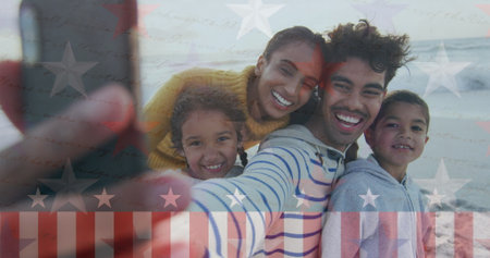 Taking family selfie on sandy ocean shoreline, showcasing smartphone with stars and stripes overlay. Family, celebration, outdoor, candid, leisure, unity, joyの写真素材