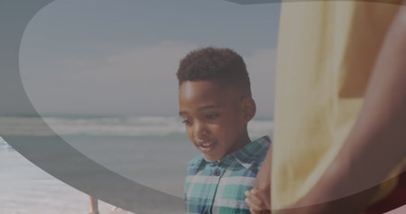Standing boy wearing green and white shirt holding adult hand, peering at waves on sandy beach. Family, seaside, tranquility, adventure, natural, connection, outdoorの写真素材