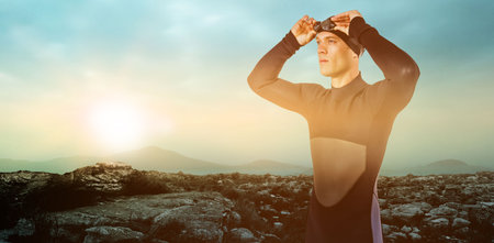 Male swimmer looking away against rocks during sunsetの写真素材