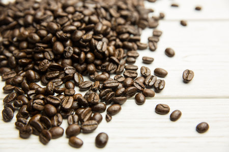 Dark roasted coffee beans spreading across pale wooden tabletop in flat design, copy space....