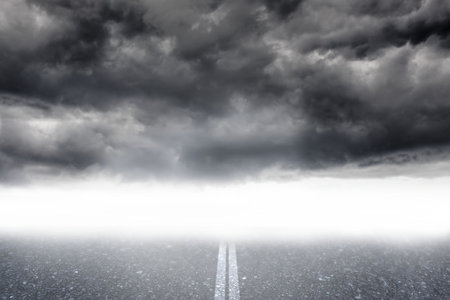 Flat design showing empty asphalt road with faded center line leading into fog under storm clouds. Deserted, moody, expansive, ominous, atmospheric, dramatic, ruggedの写真素材